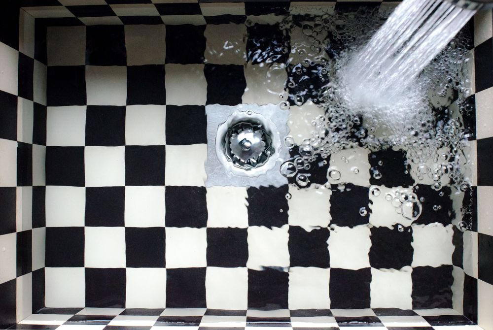 Évier à carreaux noirs et blancs avec l'eau qui s'écoule par la bonde